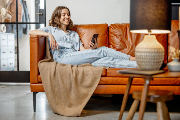 Nainen käyttää älypuhelinta istuessaan sohvalla - Valokuva, kuva