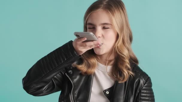 Bella ragazza adolescente bionda elegante che registra il messaggio vocale ad un amico sullo smartphone su sfondo blu. Comunicazione a distanza - Filmati, video