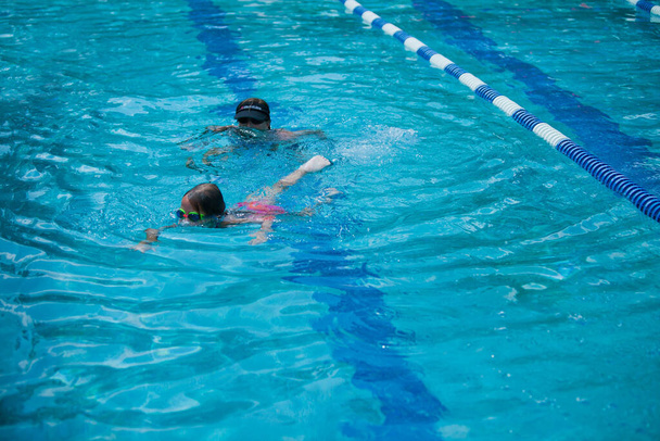 Bambina nuotare durante le sue lezioni di nuoto presso la piscina esterna locale in estate - Foto, immagini