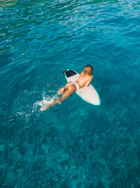 Vonzó szörfös nő, aki a kék óceán szörfdeszkáján pihen. Légi felvétel a szörfös lánnyal - Fotó, kép