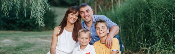 Boldog kaukázusi család négy emberrel a szabadban, nyáron. Anya és apa két fiútestvért ölelgetnek. Életmód autentikus természetes érzelmek pillanat. Web banner fejléc. - Fotó, kép