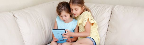Dvě bělošky se dívají na digitální tablet. Děti používající digitální přístroj. Upřímný autentický životní styl raného vývoje. Nová generace technologií. Záhlaví webového nápisu. - Fotografie, Obrázek