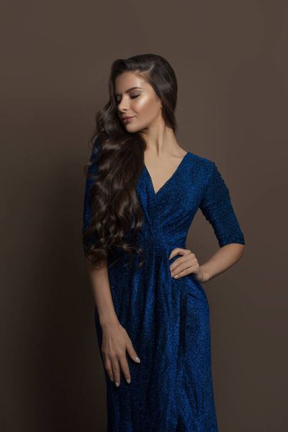 Młoda atrakcyjna brunetka nosi niebieską suknię wieczorową na brązowym tle - Zdjęcie, obraz