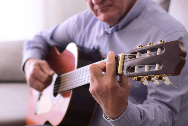 Zbliżenie gitary i ręce 60-latka grającego na gitarze. Muzyka koncepcyjna. - Zdjęcie, obraz