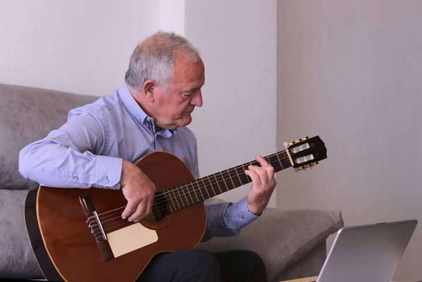 Concept μουσική σε χρόνο περιορισμού, covid19. Ώριμος άντρας παίζει κιθάρα μόνος στο σπίτι.. - Φωτογραφία, εικόνα