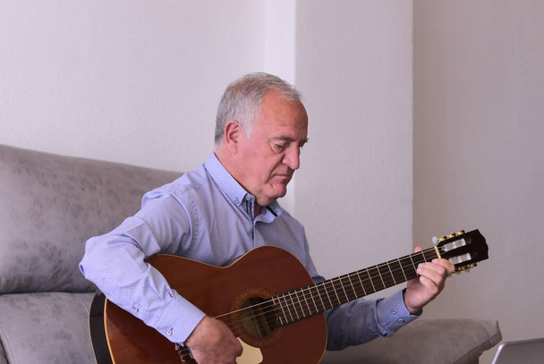 Pojem hudba v internaci, covid19. Starší muž hraje doma na kytaru sám. - Fotografie, Obrázek