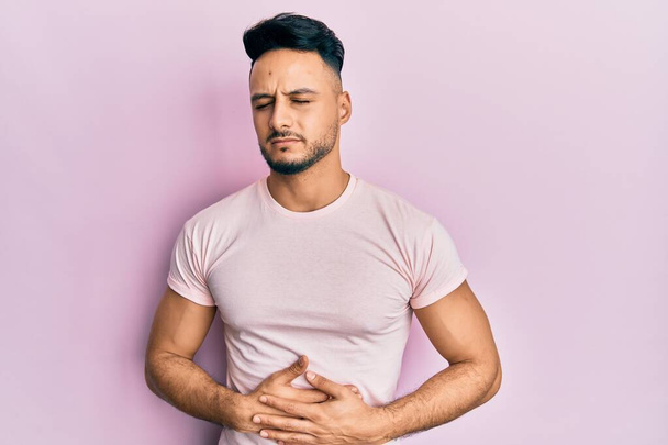 Hombre árabe joven que usa ropa casual con la mano en el estómago porque la indigestión, la enfermedad dolorosa sensación de malestar. concepto ache.  - Foto, imagen