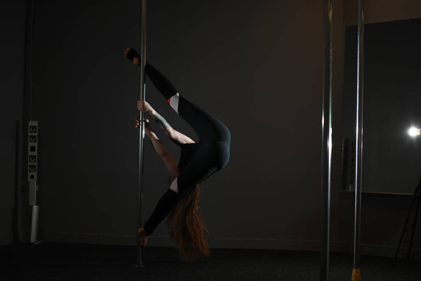 Meisje doet oefeningen op een sportuitrusting. De danser op de pyloon in de studio. - Foto, afbeelding