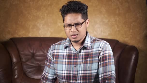  joven asiático hombre tos y estornudos sentado en un sofá  - Metraje, vídeo