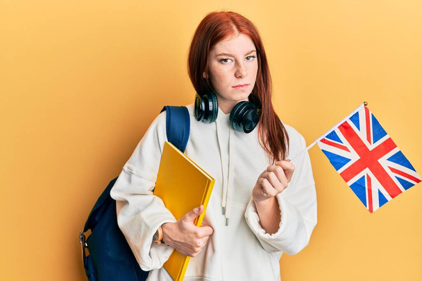Joven estudiante de intercambio de chicas cabeza roja sosteniendo bandera del Reino Unido escéptico y nervioso, frunciendo el ceño molesto debido a un problema. persona negativa.  - Foto, Imagen