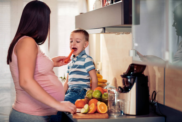 Mujer embarazada y su hijo comiendo verduras saludables. - Foto, imagen