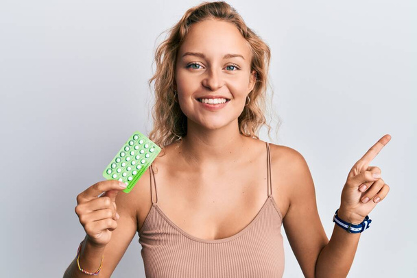 Красивая белая женщина с противозачаточными таблетками, счастливо улыбающаяся, указывая рукой и пальцем в сторону  - Фото, изображение