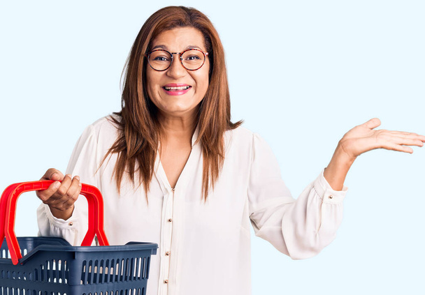 молода красива біла жінка з кошиком і візком супермаркетів над ізольованим студійним фоном
 - Фото, зображення