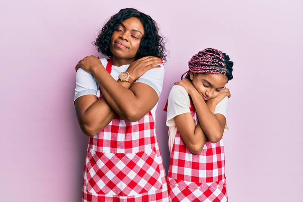 パン屋の制服を着た美しいアフリカ系アメリカ人の母親と娘は、自分自身を幸せと肯定的に抱き、自信を笑っています。自己愛と自己ケア  - 写真・画像