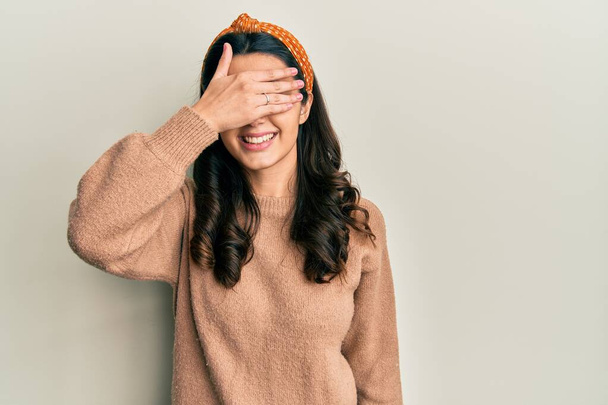 Junge hispanische Frau in lässiger Kleidung lächelt und lacht mit der Hand auf dem Gesicht, die Augen zur Überraschung verdeckt. Blindes Konzept.  - Foto, Bild