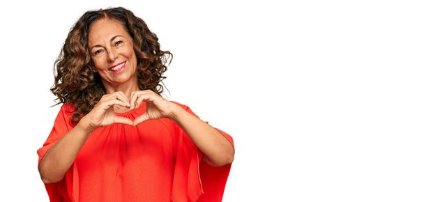 Mujer hispana de mediana edad vistiendo ropa casual sonriendo en amor mostrando el símbolo del corazón y la forma con las manos. concepto romántico.  - Foto, imagen