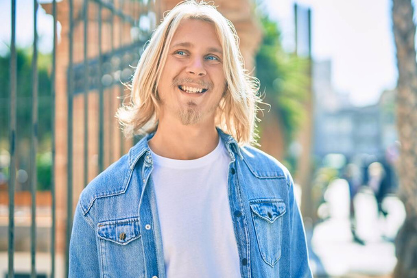 Молодий блондин скандинавський чоловік усміхається щасливий стоячи в місті
. - Фото, зображення