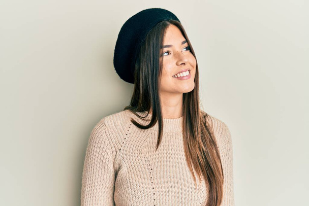 Young brunette woman wearing french look with beret looking away to side with smile on face, natural expression. laughing confident.  - Photo, Image