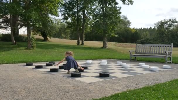Little girl is playing large outside checkers in the park. Active child, happy childhood concepts - Footage, Video