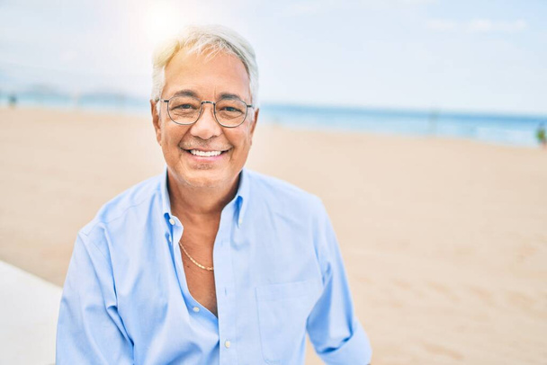 Handosme його латиноамериканський чоловік з сірим волоссям посміхається щасливим на пляжі, насолоджуючись відпусткою влітку
 - Фото, зображення