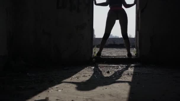 Dziewczyna tańczy twerk w drzwiach na dachu opuszczonego budynku. Dziewczyna w czerwonych spodenkach i rajstopach w celi. - Materiał filmowy, wideo
