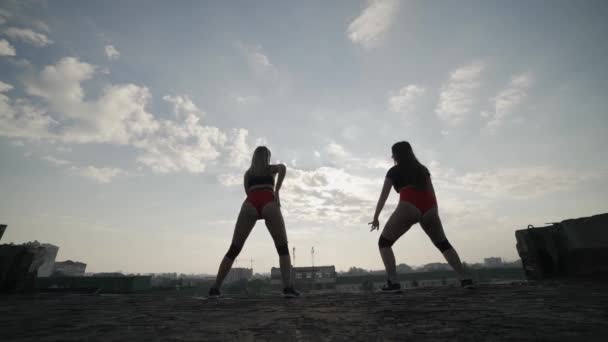 Dwie dziewczyny tańczą na dachu opuszczonego budynku. Dziewczyny w czerwonych szortach i obcisłych rajstopach. - Materiał filmowy, wideo