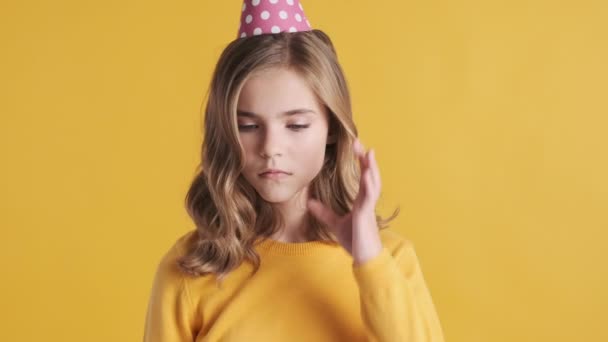 Overstuur blond tienermeisje draagt feestmuts die er verdrietig uitziet omdat het vieren van verjaardag alleen over gele achtergrond. Eenzaam meisje - Video