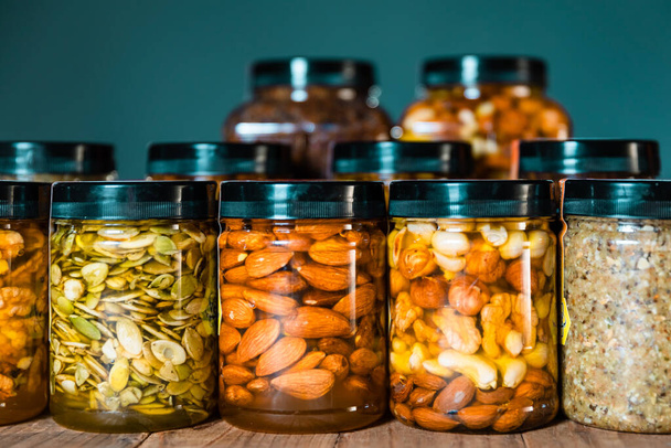 Honey mixed with nuts, seeds, dried fruits. Honey packaged in transparent jars with lids in lines or rows on wooden table. Delicious healthy food - Photo, Image