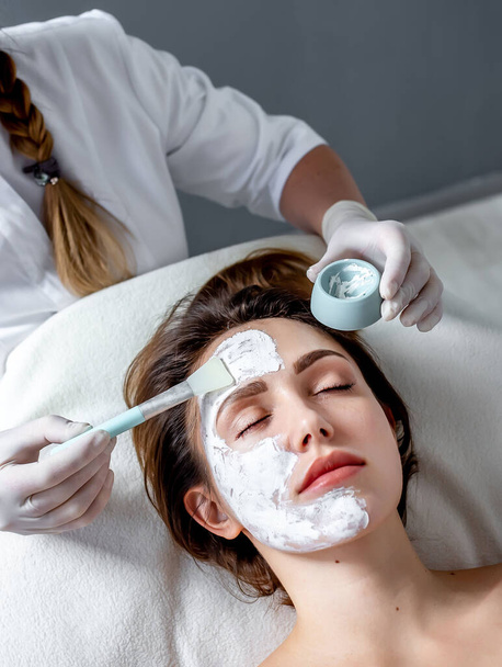 belle femme blonde dans le salon de spa ayant masque facial avec pinceau cosmétique sur la main sur la procédure de rajeunissement. - Photo, image