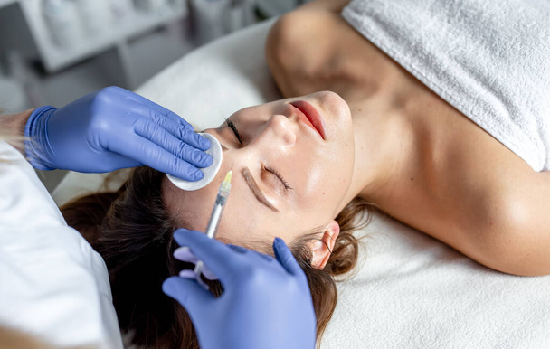 Cosmétologue faisant un traitement facial permanent. femme recevant un coup laser sur le visage d'un jeune esthéticien. - Photo, image