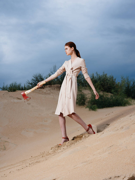 on the sand on a deserted beach a woman with an ax and a sundress - Fotografie, Obrázek