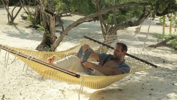 Young man with modern tablet computer relaxing on hammock - Filmati, video
