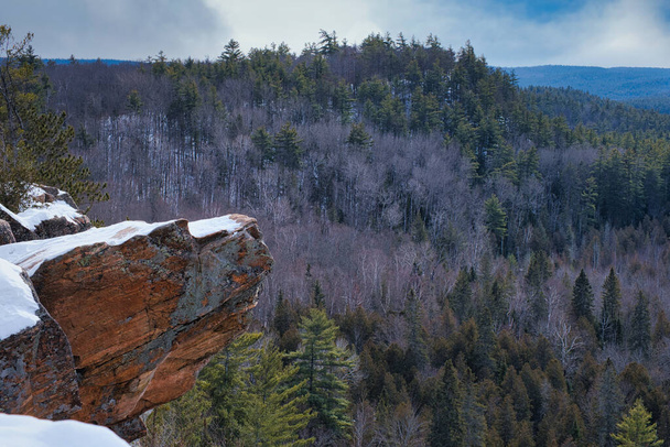 En invierno, la nieve cubre la roca que sobresale sobre el acantilado en Eagle 's Nest Lookout, Calabogie, Ontario, Canadá. Las colinas de las tierras altas del este de Ontario se ven detrás de él. - Foto, Imagen