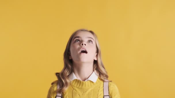 Pretty blond teenage student girl keeping thumbs up looking up on copy space for your advertisement or promotional content over yellow background. Like it gesture. Happy emotions - Footage, Video