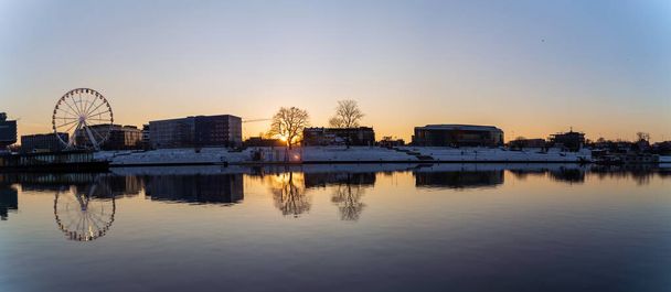 Krakov, Polsko - 31. ledna 2021: Panoramatický záběr Krakovské krajiny, ruského kola a polské architektury vedle řeky Visly při západu slunce v zimě. - Fotografie, Obrázek