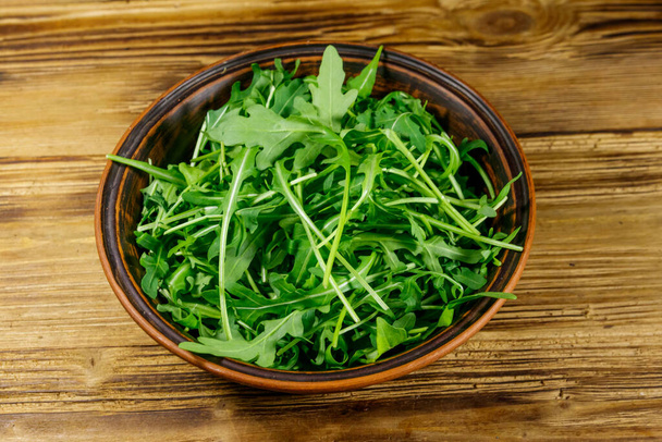 Friss zöld arugula kerámia tálban egy fa asztalon. Egészséges étel vagy vegetáriánus fogalom - Fotó, kép