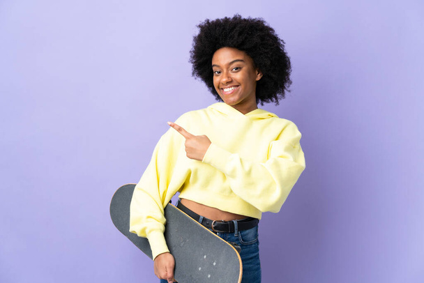 Young African American woman isolated on purple background with a skate and pointing to the side - Foto, afbeelding