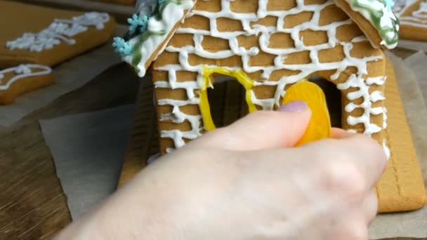 Gingerbread frosting. Chefs female hands decorate with yellow sugar icing and pastry shop with a bag of gingerbread house in the home kitchen. New year traditions - Footage, Video