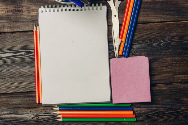 notatniki kolorowe ołówki długopisy nożyczki na drewnianym tle widok z góry - Zdjęcie, obraz