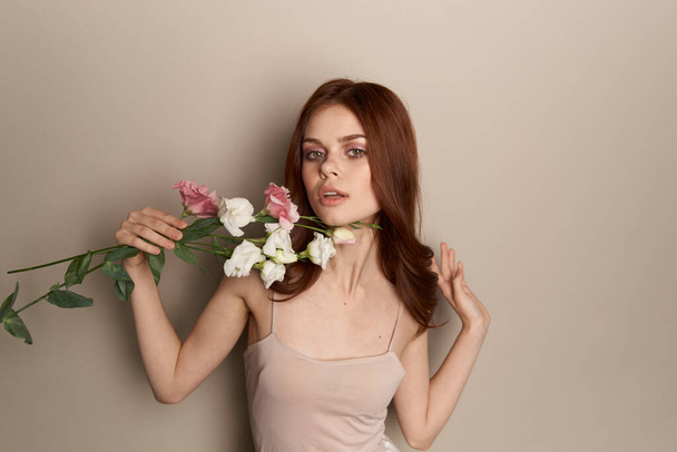 Mujer feliz con un ramo de flores ligeras sobre un fondo beige hombros desnudos modelo pelo rojo hermosa cara - Foto, imagen