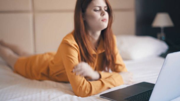 γυναίκα βρίσκεται στο κρεβάτι μπροστά από το φορητό υπολογιστή συναισθήματα τεχνολογία freelance - Φωτογραφία, εικόνα