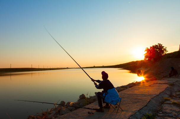 Young man fishing on a lake with colorful background - Photo, Image