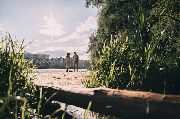 happy young couple of people run near the lake holding hands and throwing stones into the water. lovely girl with a guy in nature are walking. romantic date - Foto, imagen