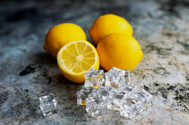 Чотири лимони і кубики льоду на сірому фоні. Лимон нарізаний. Свіжі фрукти
. - Фото, зображення