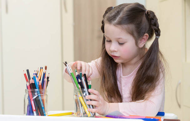 Uma garotinha fofa desenha enquanto se senta na mesa, a criança escreve com lápis em um álbum, criatividade infantil, desenvolvimento precoce, terapia de arte, educação pré-escolar. - Foto, Imagem