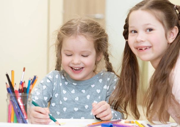 Две красивые девочки рисуют карандашами, дети занимаются творчеством, ранним развитием, обучением детей. - Фото, изображение