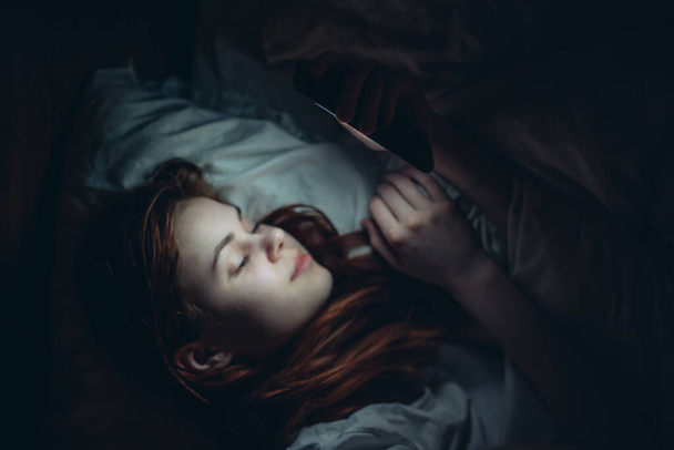 pretty woman lying in bed at night with phone before bedtime addiction - Photo, Image