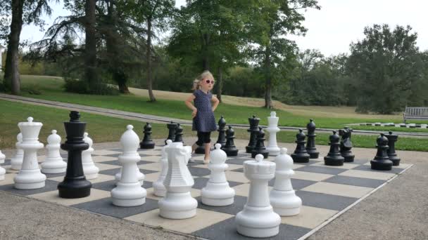 小さな女の子が公園で大きな外のチェスをしている。積極的な子供、幸せな子供時代のコンセプト - 映像、動画