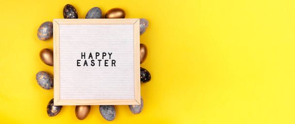 Koristeltu kulta pääsiäismunia ja kirjelauta Hyvää pääsiäistä kirkkaan keltainen loma tausta. Ylhäältä vaakasuora näkymä. - Valokuva, kuva