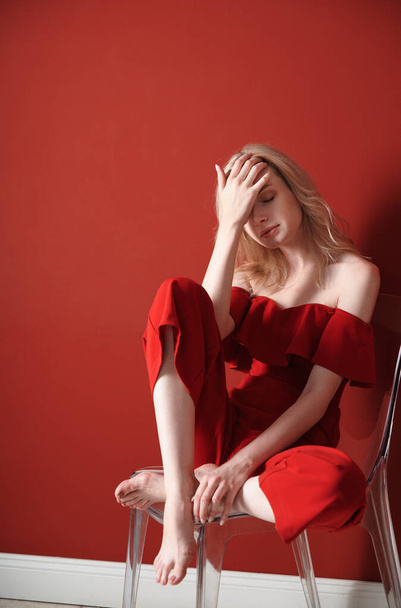 Beautiful young adult woman wearing red jumpsuit relaxing on chair - Valokuva, kuva